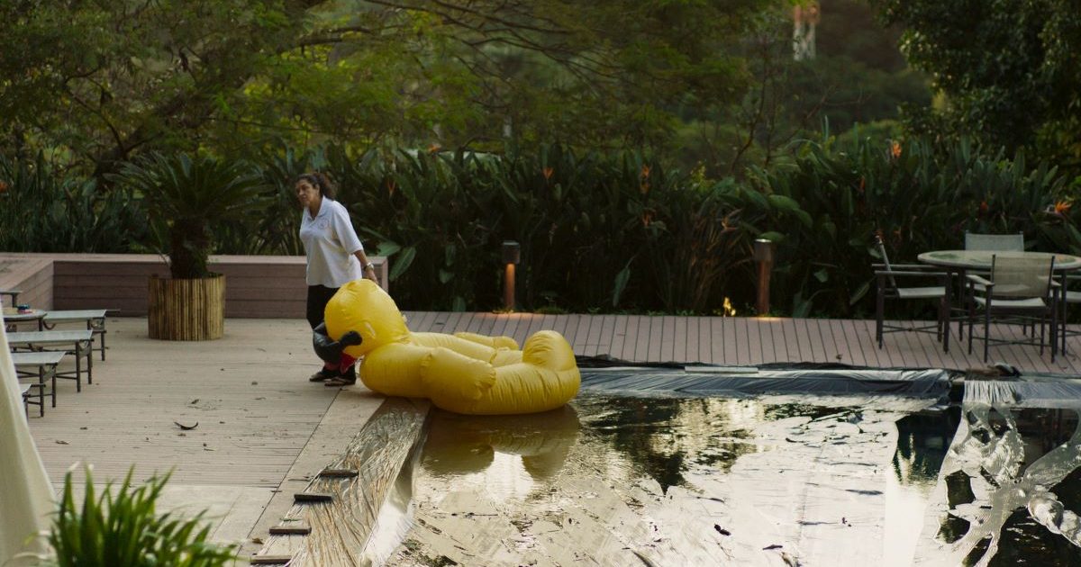 Cena do filme Três Verões, de Sandra Kogut: Regina Casé à beira de uma piscina puxando uma bóia em forma de pato amarelo