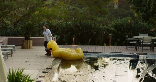 Cena do filme Três Verões, de Sandra Kogut: Regina Casé à beira de uma piscina puxando uma bóia em forma de pato amarelo